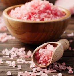 Pink sodium BHB mineral crystals displayed in wooden bowl with scoop on rustic wooden table.